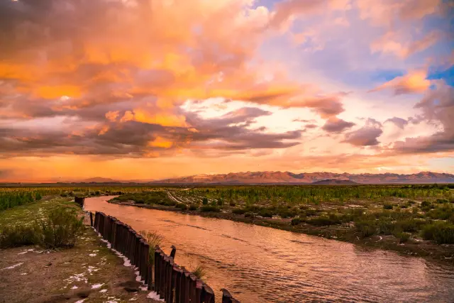 A dramatic orange sunset over a winding river with distant mountains