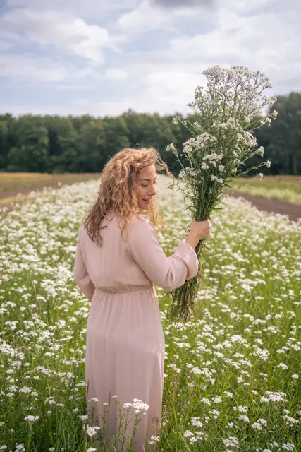 A woman walking through a field of daisies.